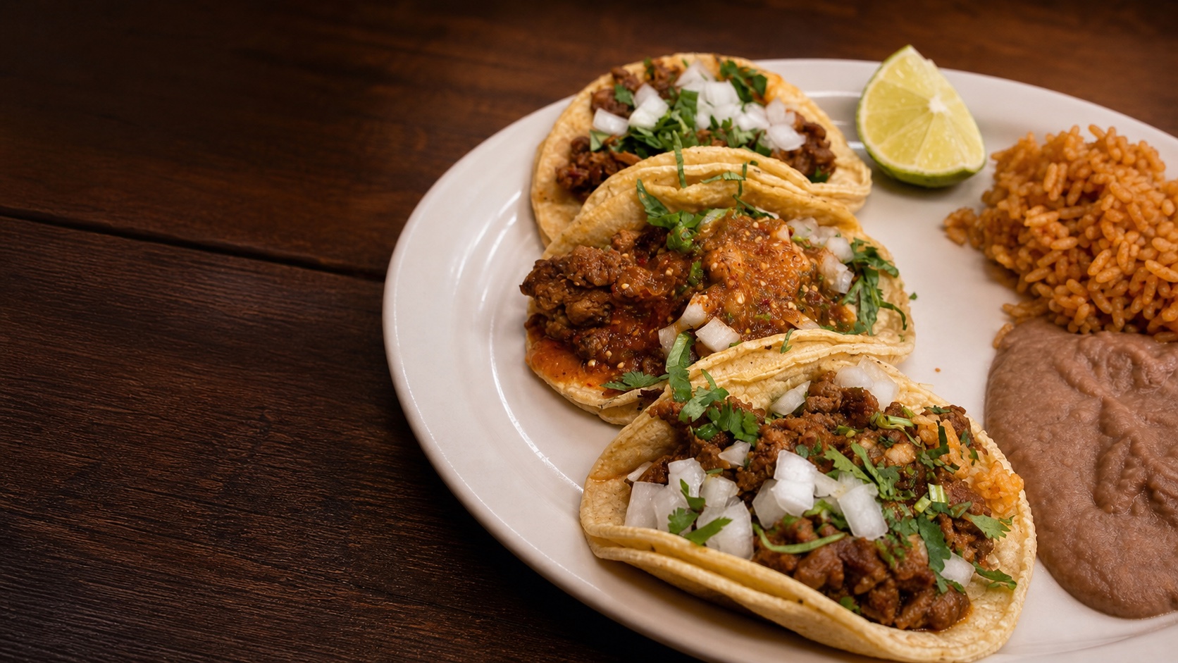 Three tacos served with rice, beans, cilantro, onion, salsa, and lime